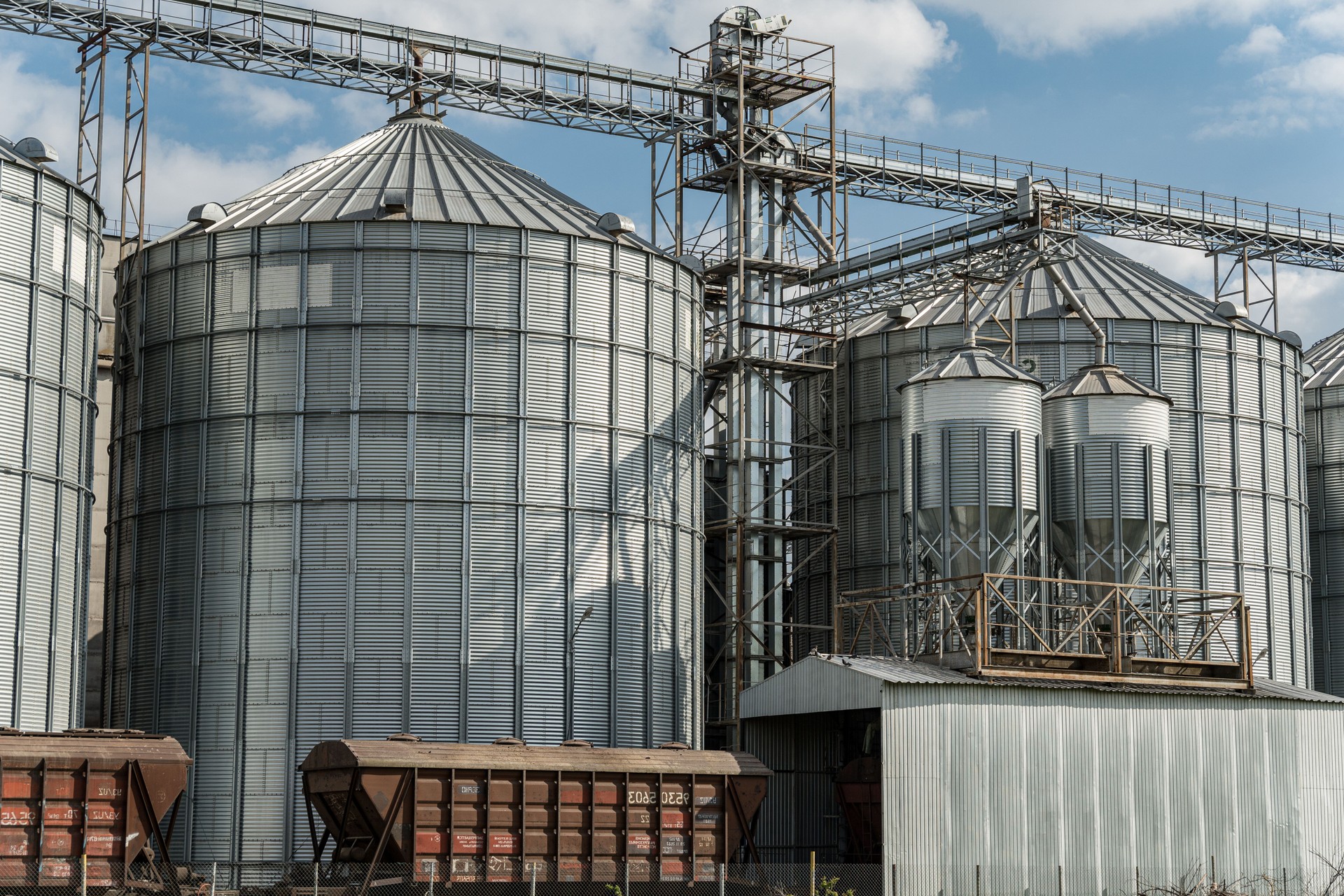 Large silos stand at an agricultural facility, storing harvested grain and crops in a rural area under a bright sky